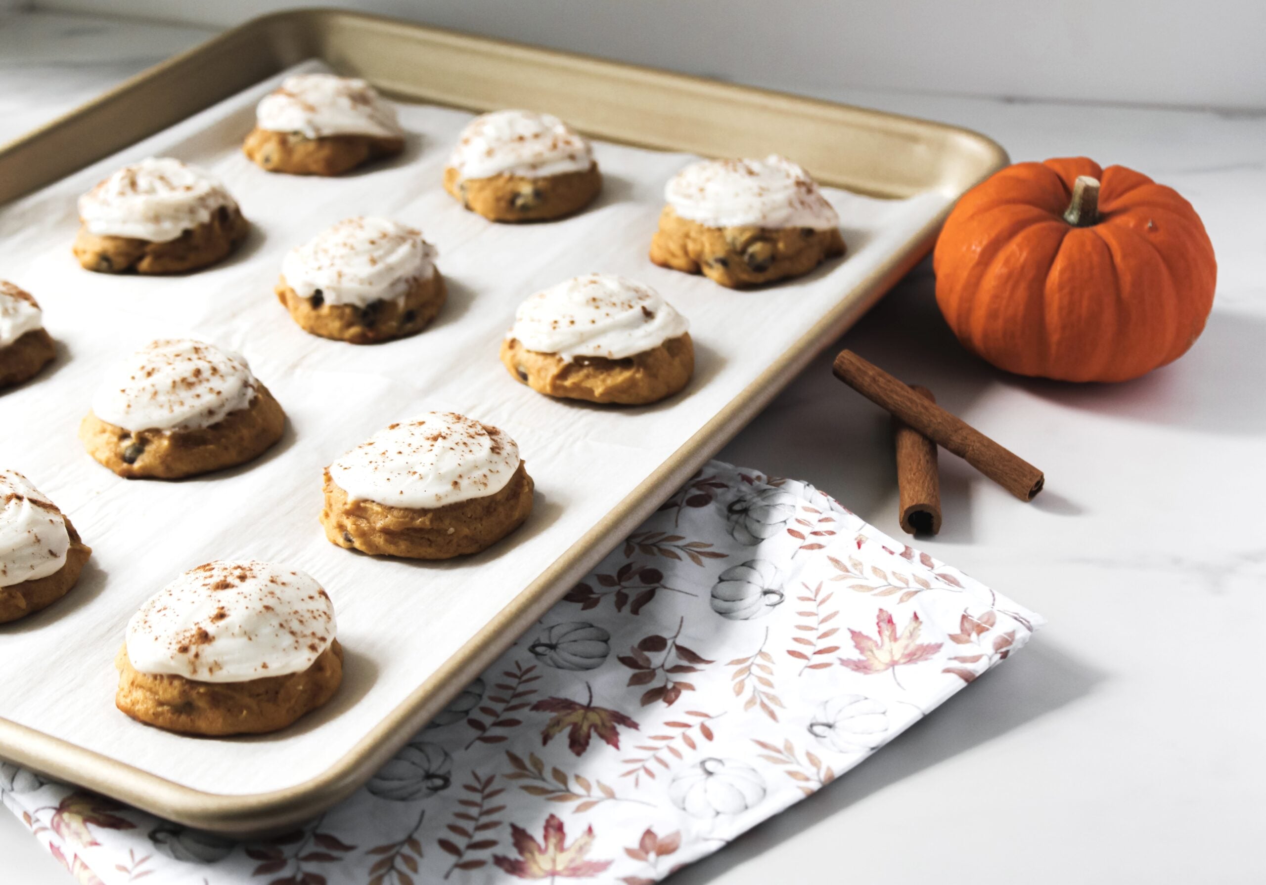 Easy pumpkin chocolate chip cookies from scratch, frosted with cream cheese frosting fully baked on a baking sheet.