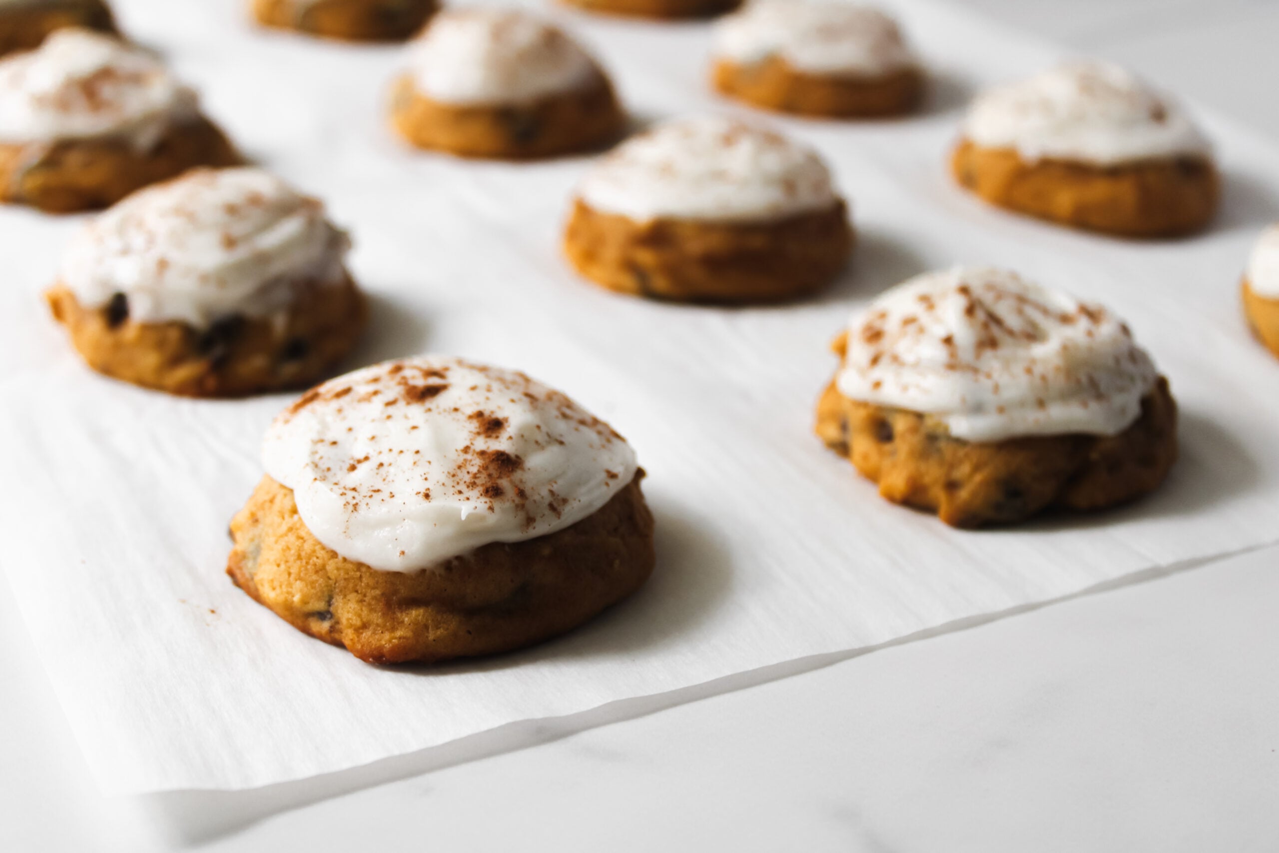 Easy pumpkin chocolate chip cookies from scratch, frosted with cream cheese frosting fully baked on a piece of parchment paper.
