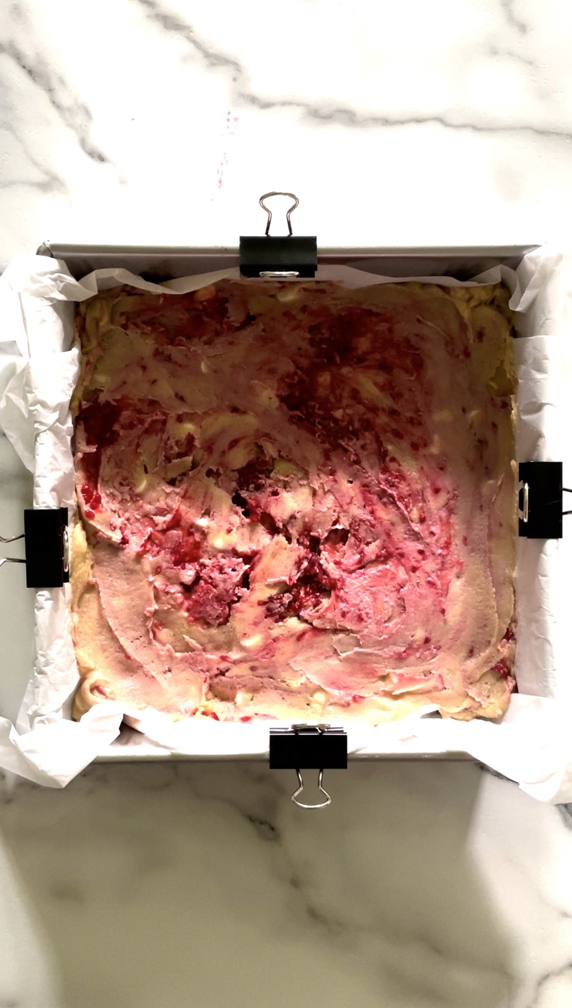 White chocolate raspberry blondies in a pan with parchment paper.