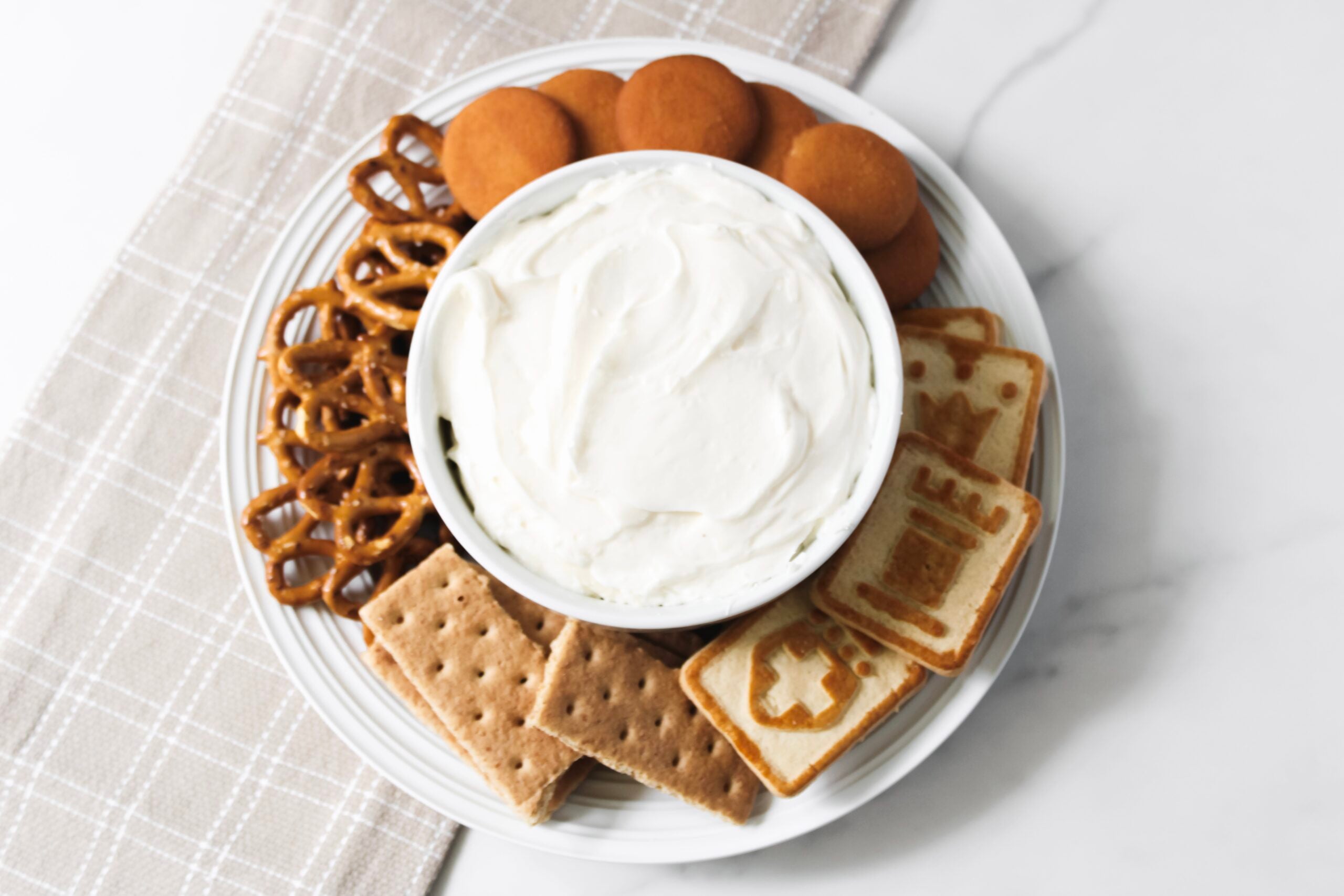 Cheesecake dip with cookies and pretzels in a bowl with towel.