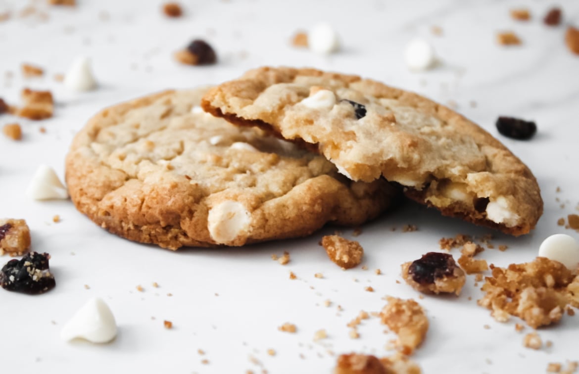 Two fully baked cranberry white chocolate chip cookies on parchment paper.