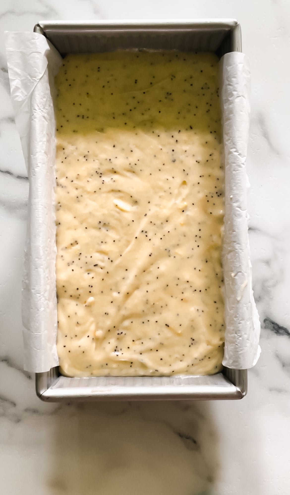 Lemon poppy seed batter in a metal baking pan lined with parchment paper.