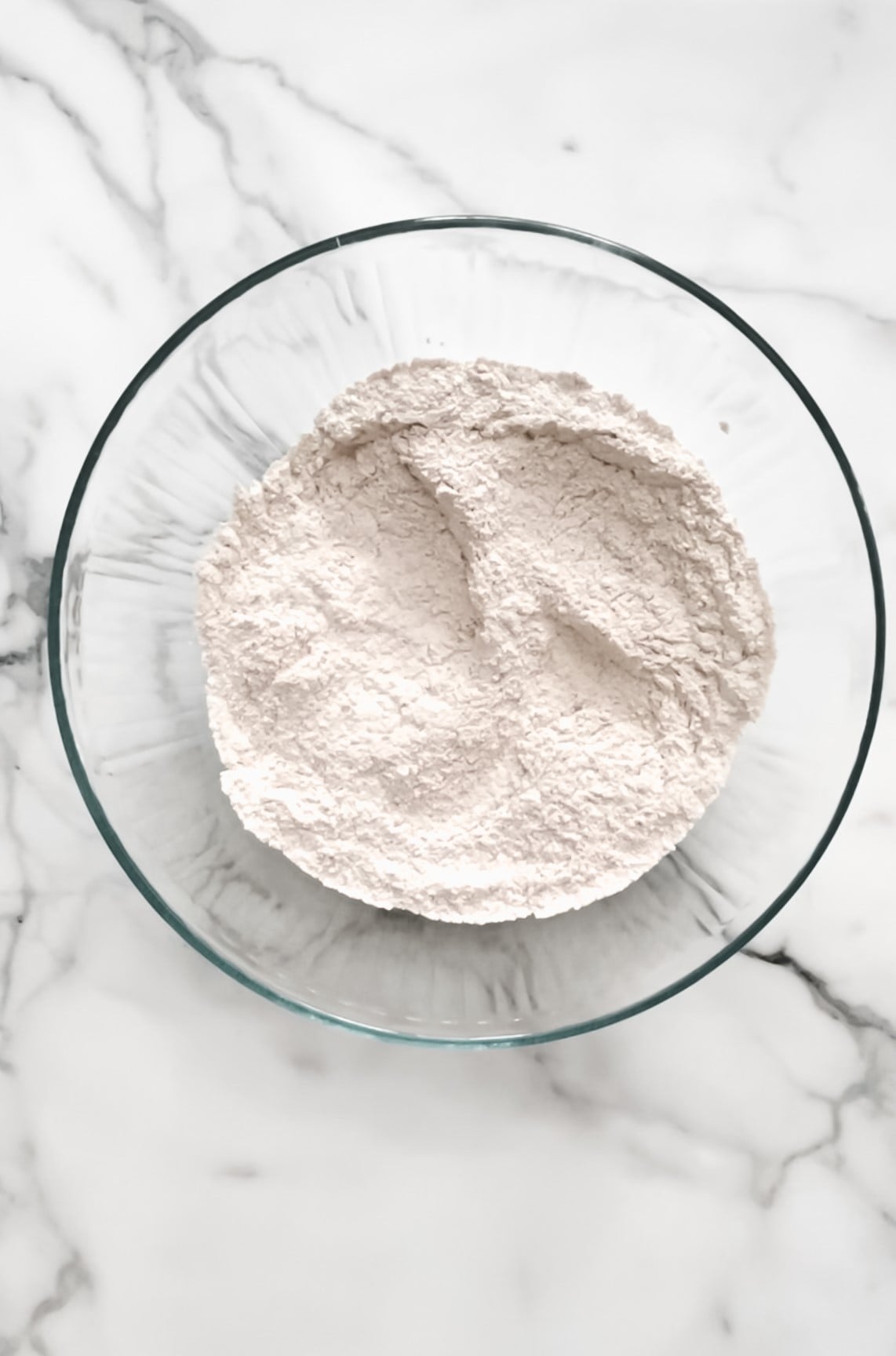 Large mixing bowl with, flour, baking powder, salt, nutmeg, and cinnamon.