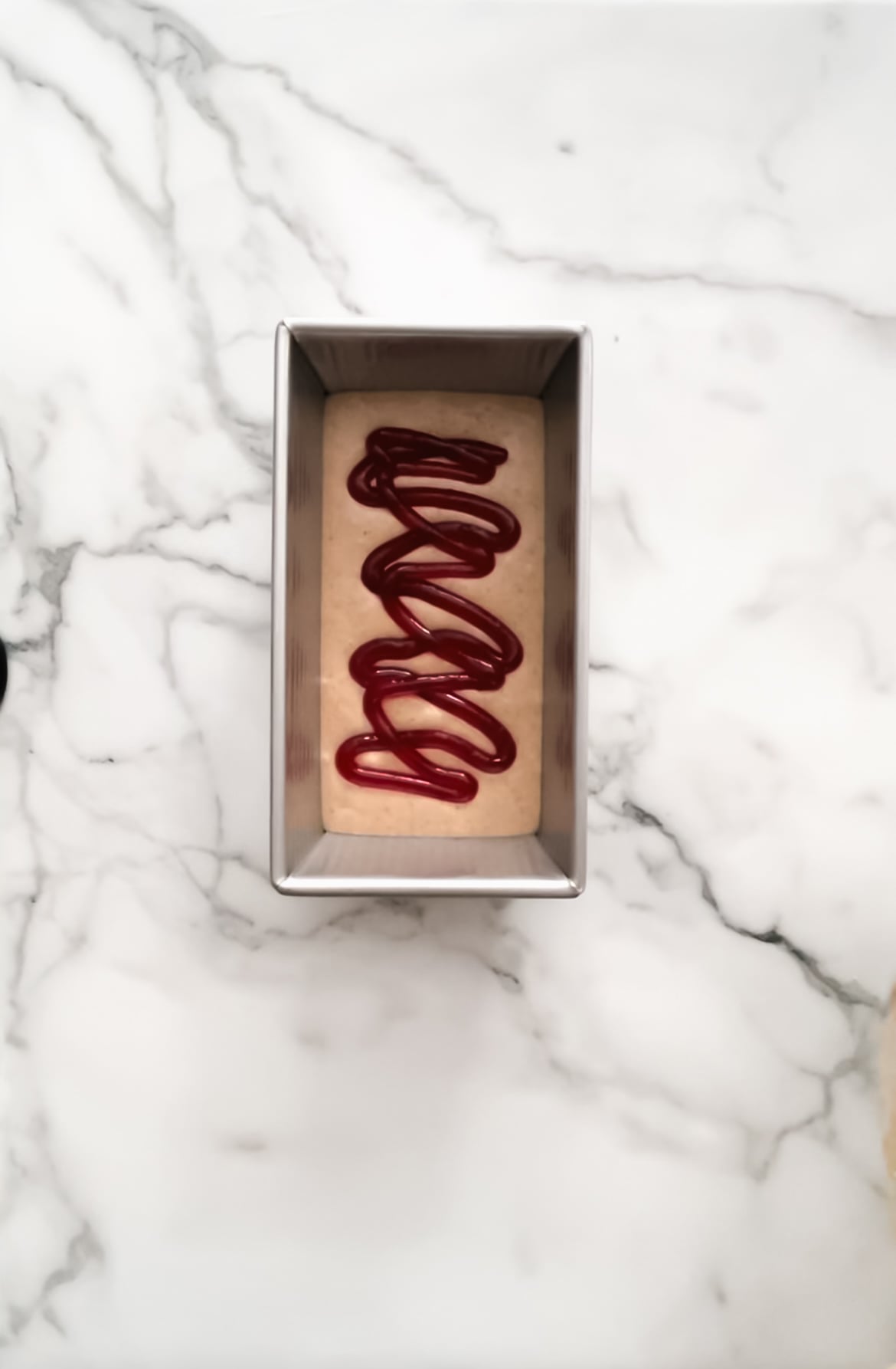 Metal loaf pan with bread batter and raspberry jam.