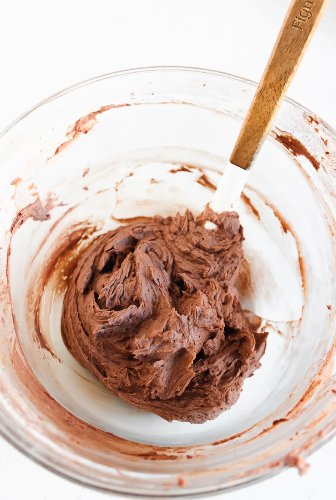 Butter, powdered sugar, hot chocolate, cocoa powder, and heavy cream in a bowl with a spatula.