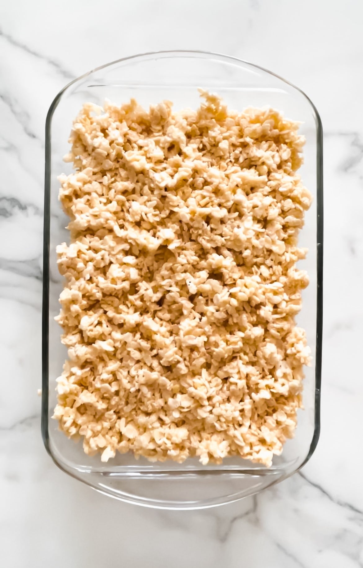 Rice Crispy cereal in a glass pan with butter, salt and marshmallows.