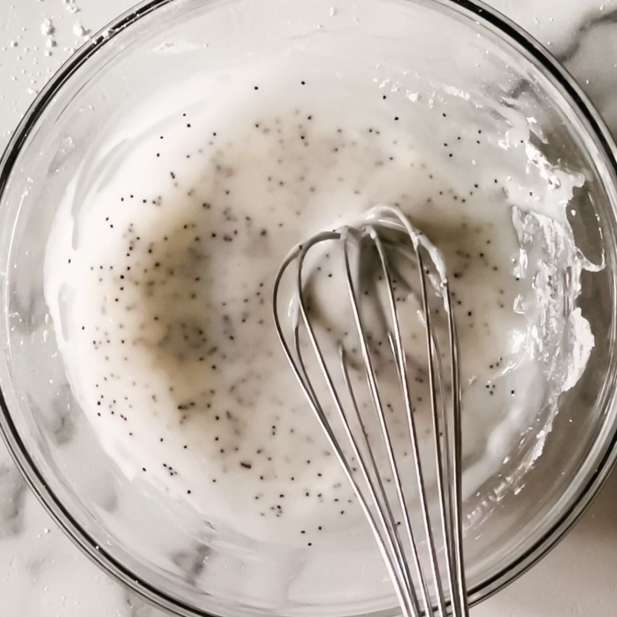 Powdered sugar, lemon juice, and poppy seeds in a bowl with a whisk.