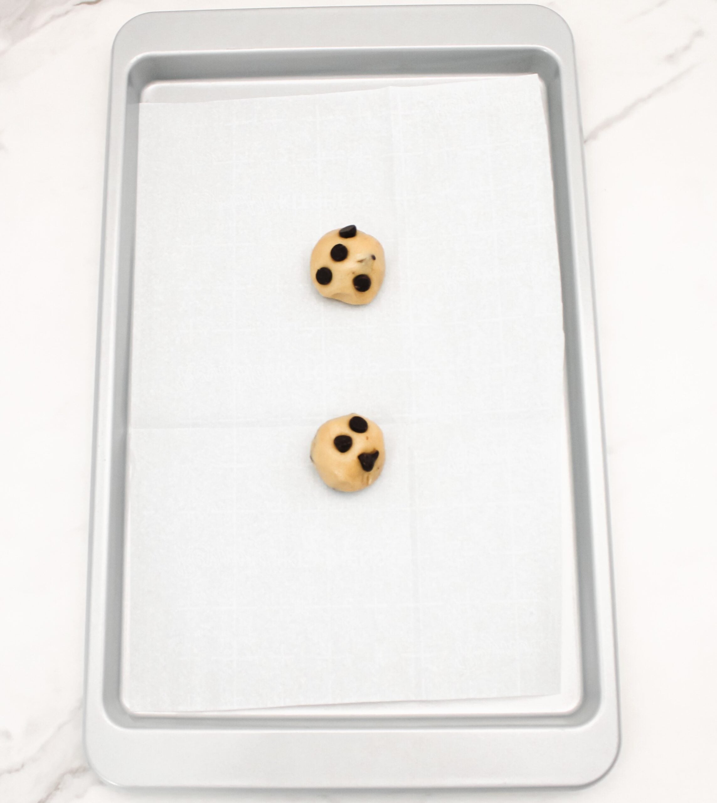 Chocolate chip cookie dough on a parchment lined baking sheet.