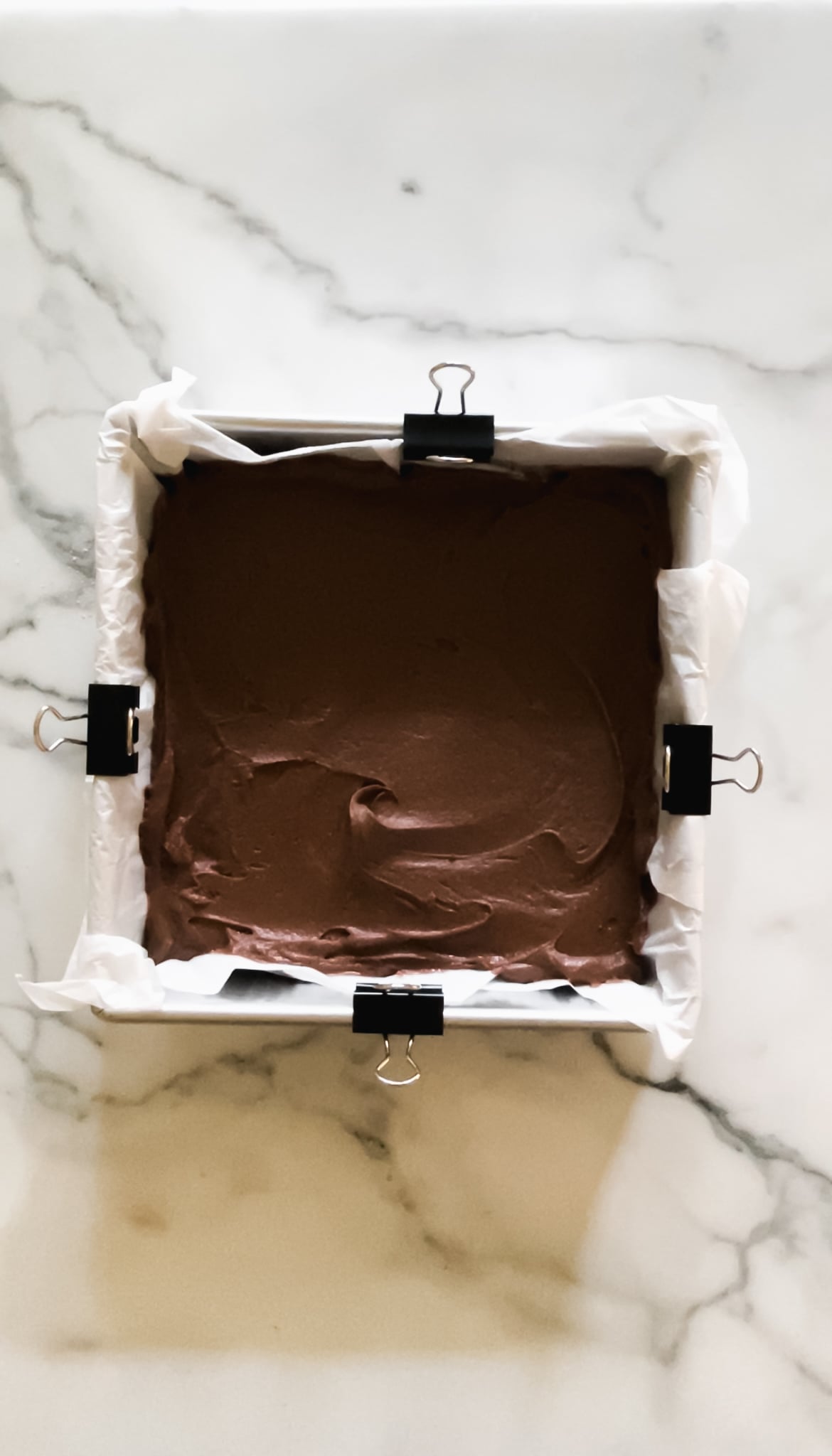 Brownie batter in a metal baking pan with parchment paper.