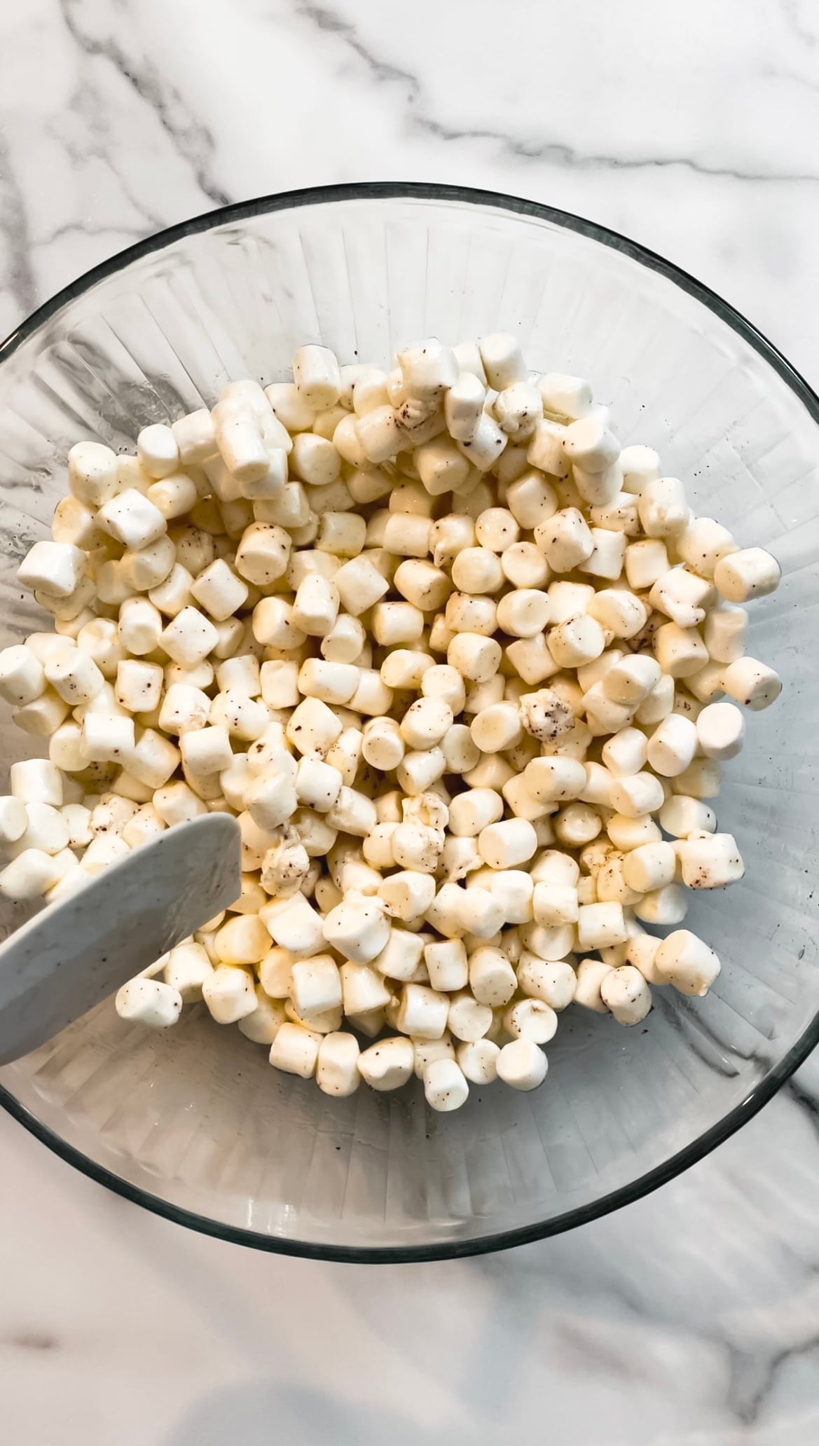 Marshmallows and butter in a glass bowl with a spatula.