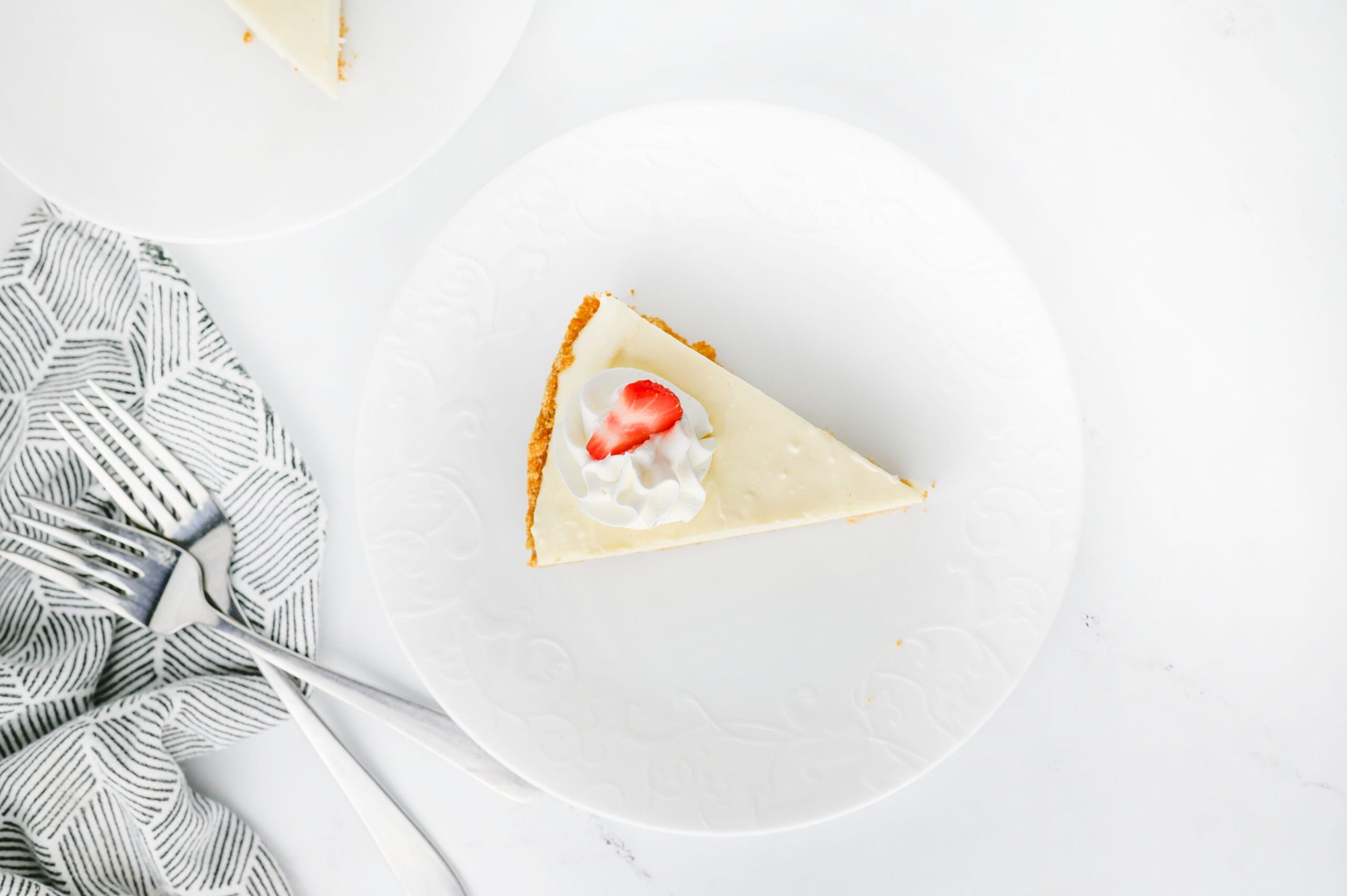 Fully prepared no-bake cheesecake on a plate with strawberries, cream, fork, and napkins.
