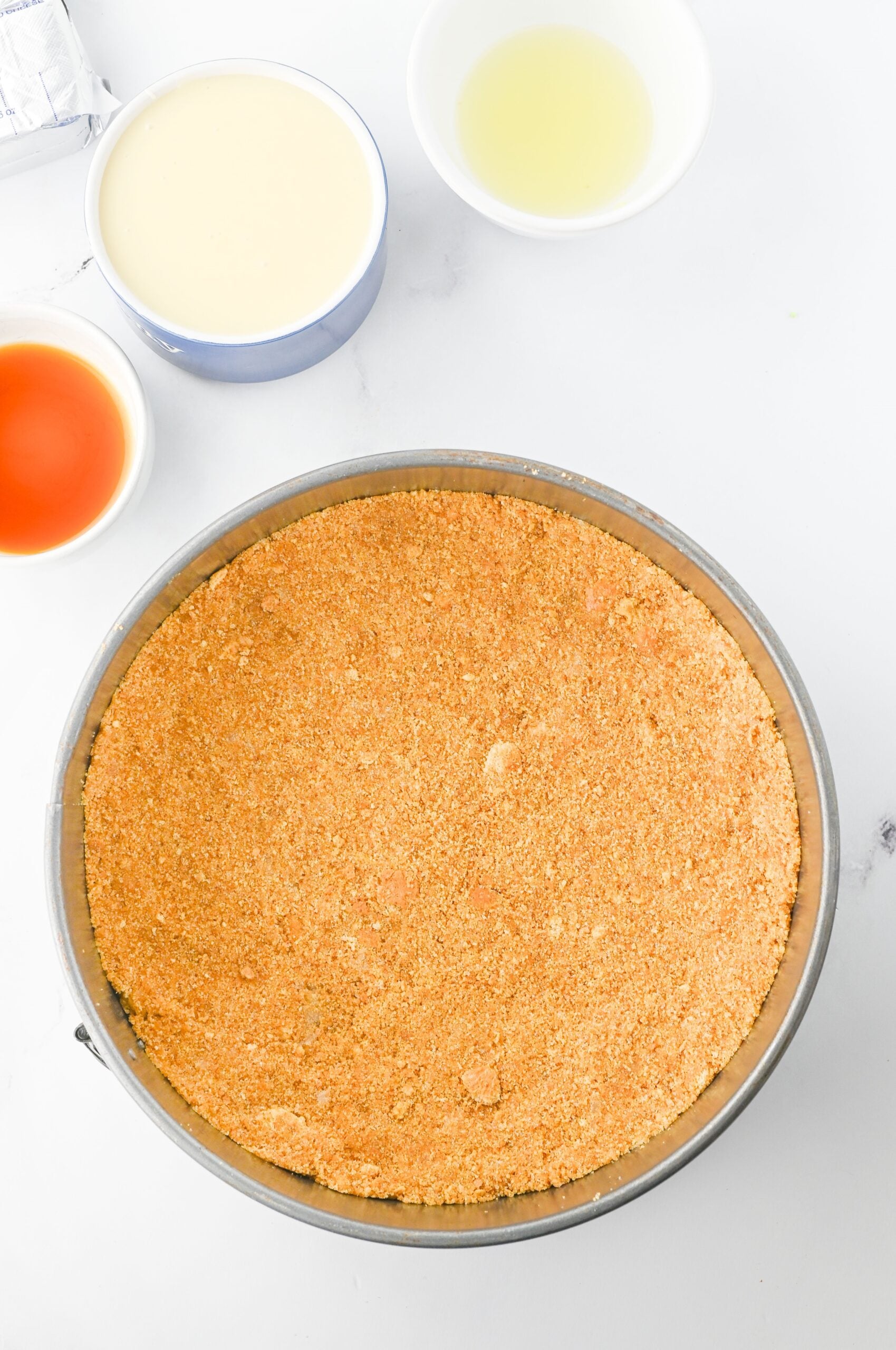 Graham crackers, vanilla, sweetened condensed milk, and lemon juice in bowls and a pie dish.