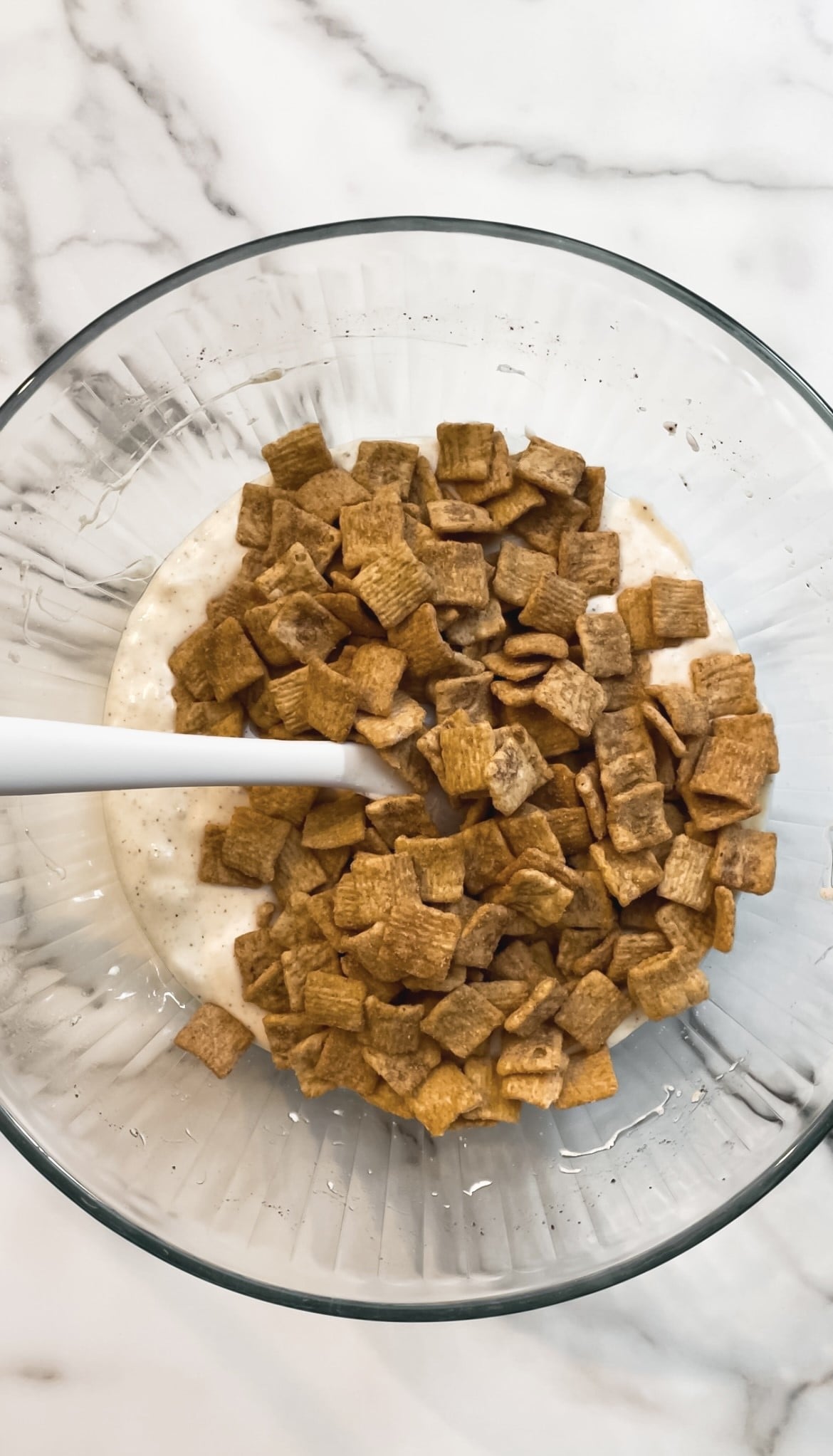 Marshmallows, butter, and cinnamon toast crunch cereal in a glass bowl with a spatula.